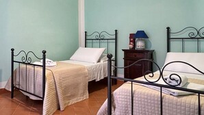 Une chambre avec deux lits, chacun doté d’un oreiller blanc et d’une couverture beige. On y trouve une table de chevet avec une lampe et un petit objet décoratif.