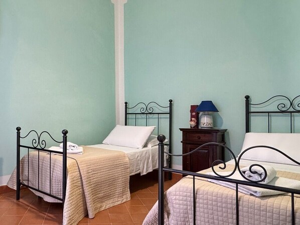 A room with two beds, each with a white pillow and a beige blanket. There is a nightstand with a lamp and a small decorative item.