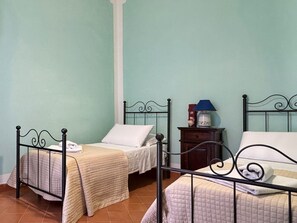 Una habitación con dos camas, cada una con un almohadón blanco y una manta color beige. Hay una mesita de noche con una lámpara y un objeto decorativo pequeño.