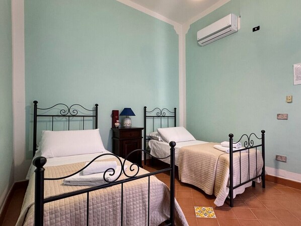Habitación con dos camas, una mesita de noche, aire acondicionado y un interruptor de luz en la pared.