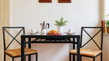 Un'area pranzo con un tavolo nero, due sedie, una moka, un croissant e una pianta in vaso.
