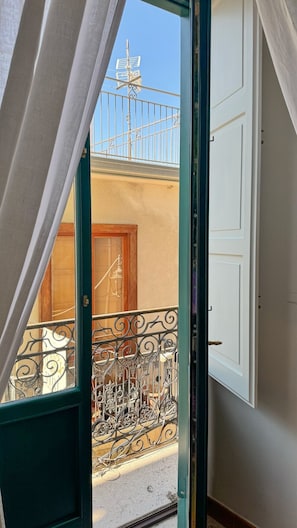 A balcony with a metal railing, a door, and a view of a building with a window and antenna.
