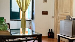 Une pièce comprenant une table à manger, des chaises, un réfrigérateur et une fenêtre avec des rideaux.