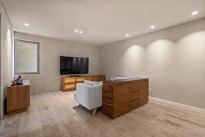 Ein modernes Wohnzimmer mit einem Flachbildfernseher, einem grauen Sofa, Holzschränken und einem Holztisch.