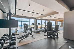 A modern gym with various exercise equipment, large windows, and a view of the outdoors. - Oceanfront Penthouse with Private Rooftop Pool (Higuera Blanca)