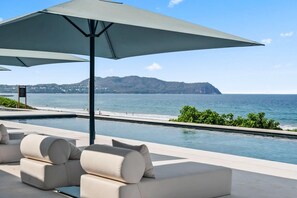 A poolside area with lounge chairs and umbrellas, overlooking a body of water and distant land. - Oceanfront Penthouse with Private Rooftop Pool (Higuera Blanca)