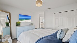 A bedroom with a bed, a dresser, a television, and a door. - Coastal Retreat- steps from the beach, pool included (Gulf Shores)