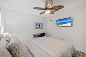 Ein Schlafzimmer mit Bett, Schreibtisch, Stuhl, Deckenventilator, Fernseher und Fenster.
