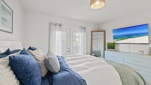 Una camera da letto con un letto, una cassettiera, uno specchio e una TV che mostra una spiaggia.