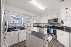 A modern kitchen with white cabinets, a stainless steel refrigerator, a microwave, an oven, and a dishwasher. - Coastal Retreat- steps from the beach, pool included (Gulf Shores)