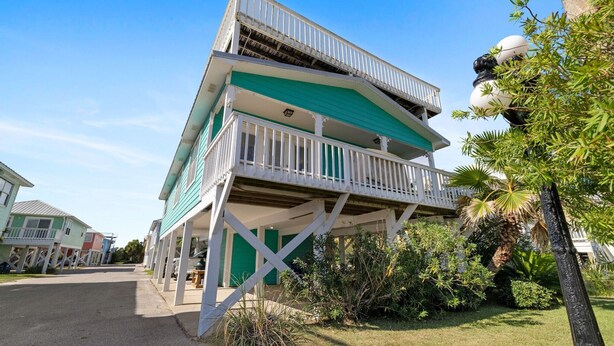 A multi-story building with a balcony on the second level, surrounded by greenery. - Coastal Retreat- steps from the beach, pool included (Gulf Shores)