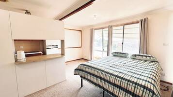 A compact room with a bed, a kitchenette, and a large window.