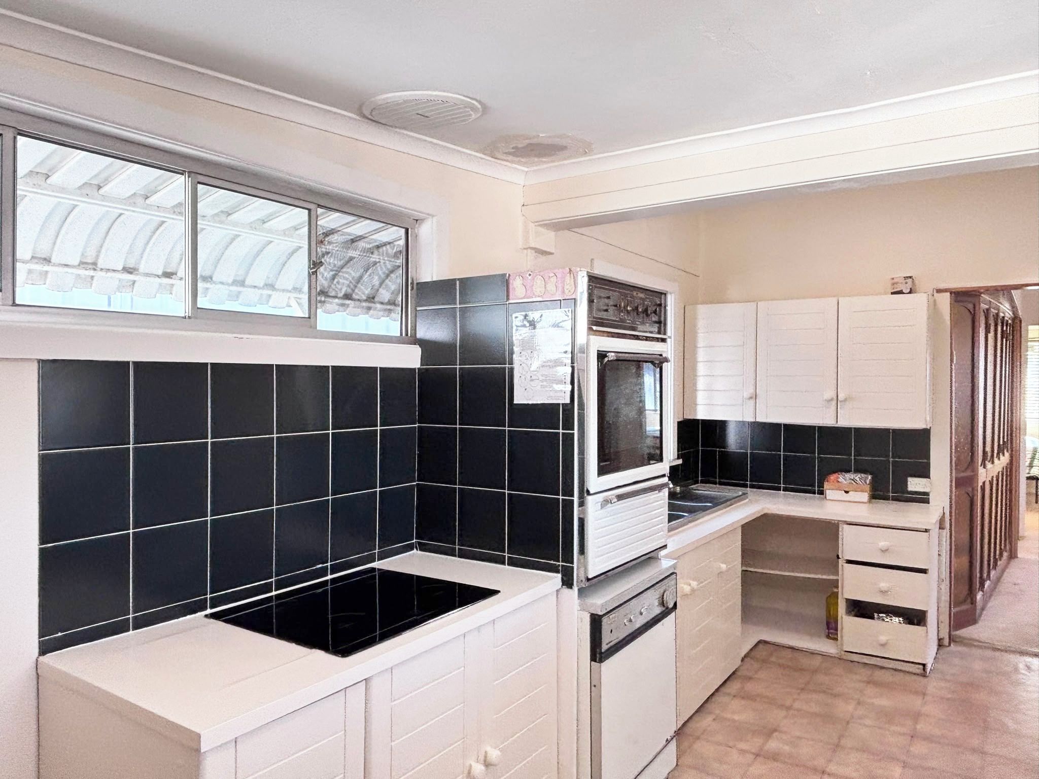 A kitchen with black and white tiles, a built-in oven, and a window with a view of the roof.
