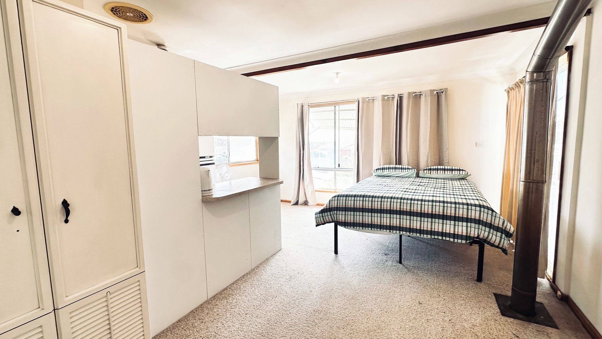 A bedroom with a bed, wardrobe, and a window with curtains.