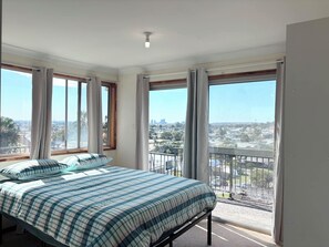 Une chambre à coucher avec un grand lit, de nombreuses fenêtres et un balcon offrant une vue sur la ville.