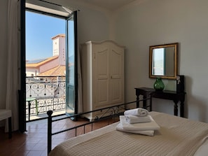 Quarto de hotel com cama, guarda-roupa, mesa pequena com um vaso e varanda com vista para edifícios.
