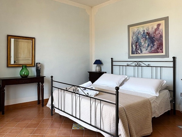 Quarto com cama, mesa de cabeceira, abajur, espelho e um quadro na parede.