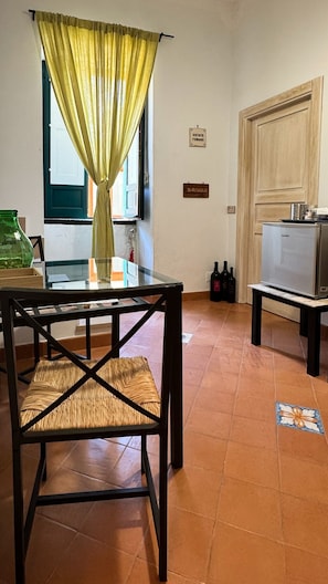 Quarto com mesa de jantar, cadeiras, geladeira e janela com cortinas.