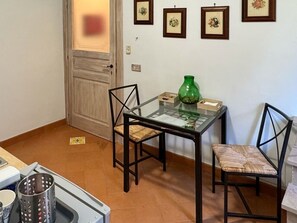 A small kitchen with a dining table, two chairs, a green vase, and a tiled floor.