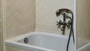 A bathroom with a bathtub, a shower, and a green tiled floor.