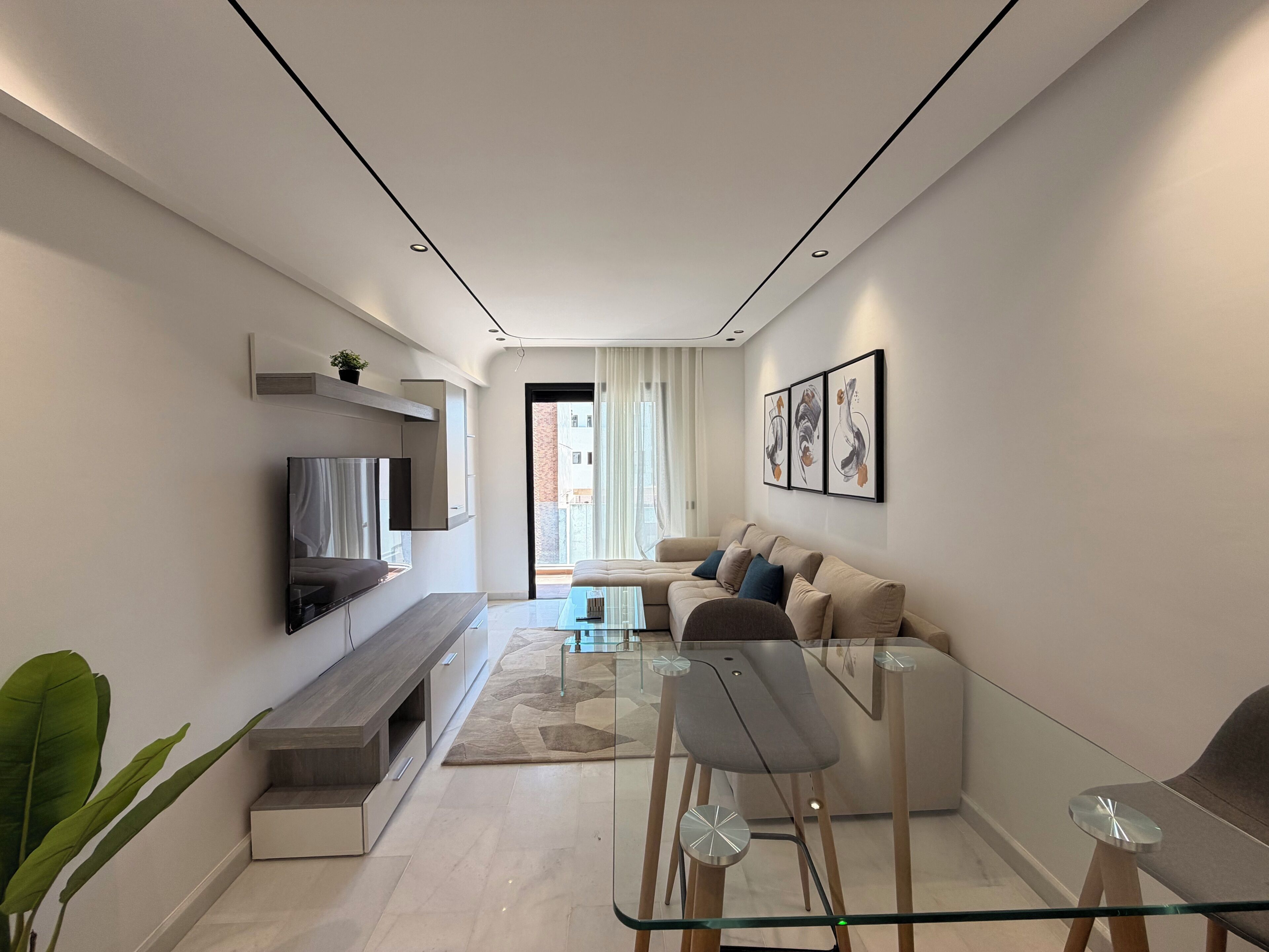 A modern living room with a sofa, a glass coffee table, and a TV mounted on the wall.