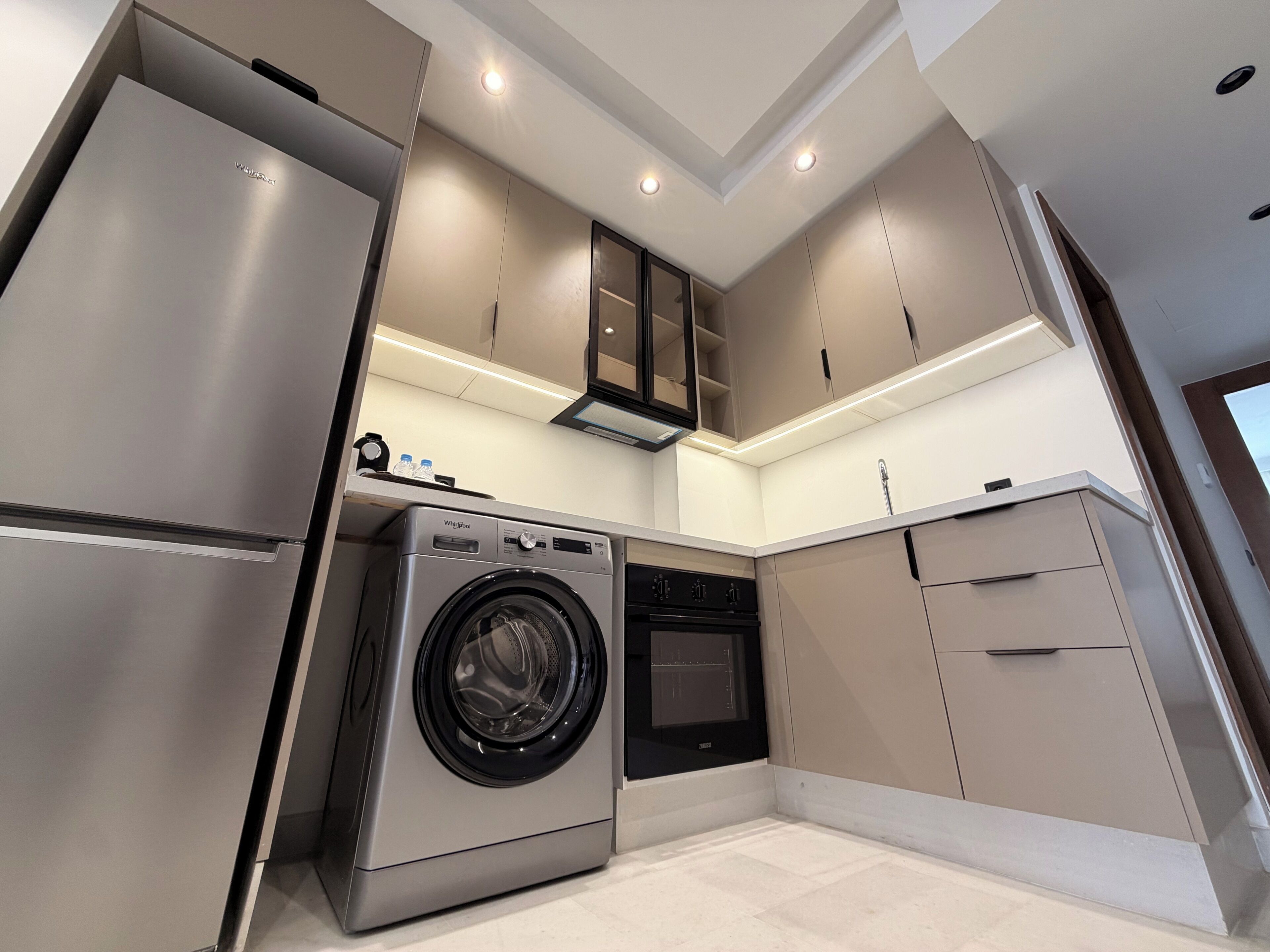 Une cuisine moderne dotée d’appareils électroménagers intégrés, notamment un réfrigérateur en acier inoxydable, un lave-linge et un four.