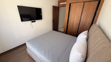 Un dormitorio con una cama, televisión montada en la pared y un armario de madera.