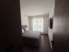 Un dormitorio con cama, televisor en la pared y ventana con cortinas.
