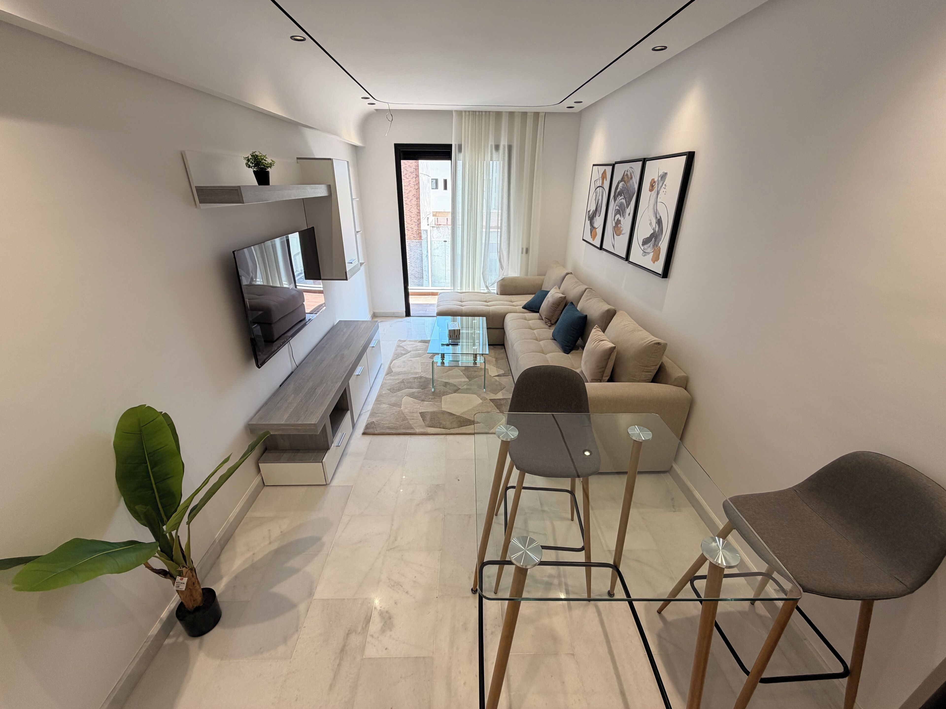 Una sala de estar moderna con sofá, mesa de centro, televisor y comedor con sillas.