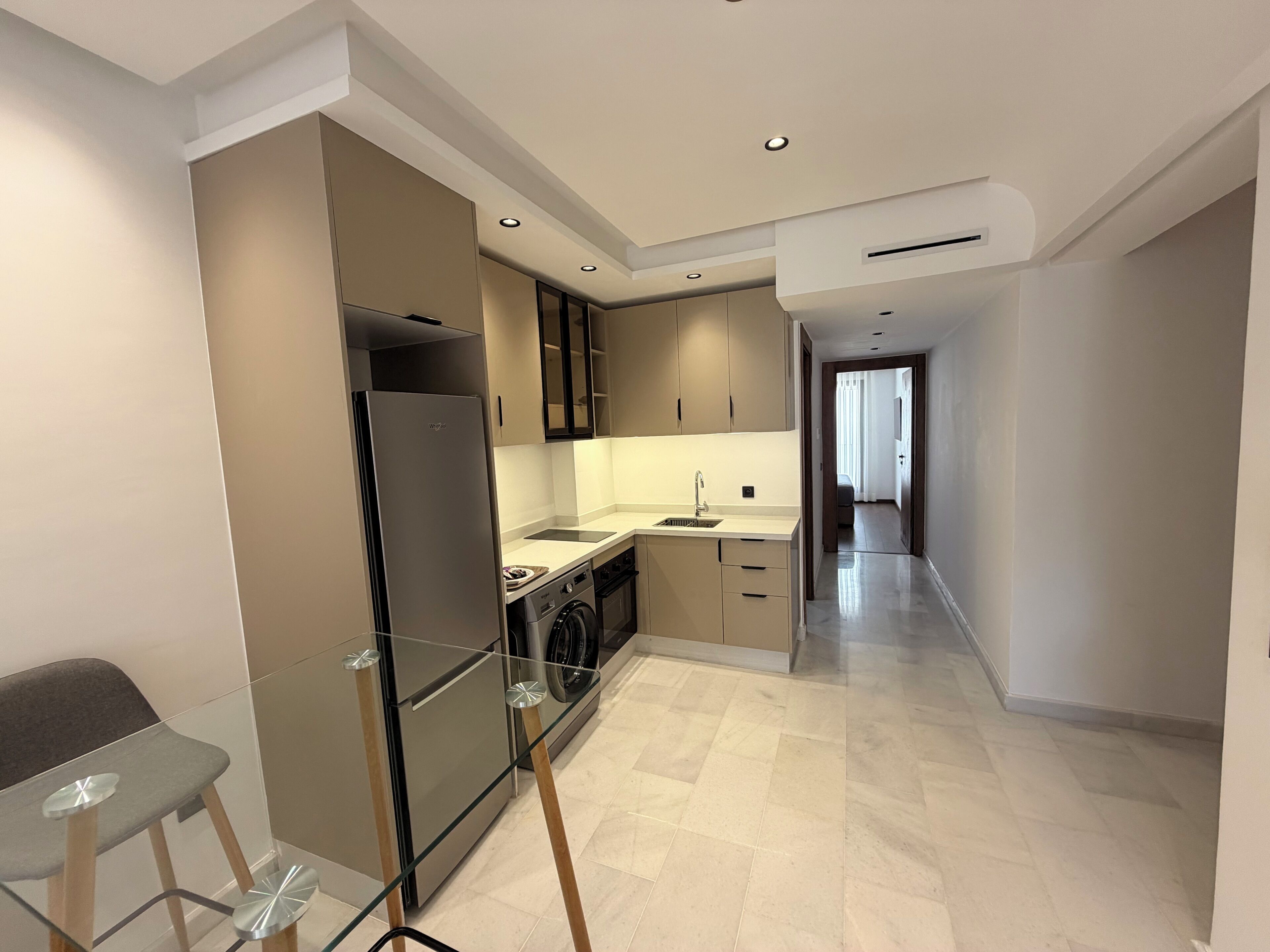 Una cocina moderna con refrigerador, lavadora y un taburete de bar de vidrio.