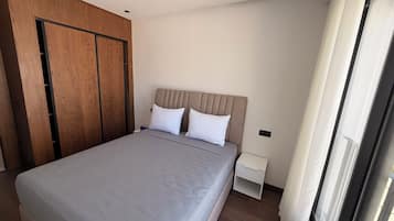 A bedroom with a large bed, wooden wardrobe, and a nightstand.