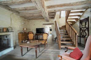 A rustic interior with exposed wooden beams, a fireplace, a television, and a staircase leading to an upper level.