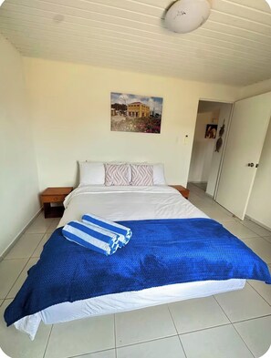 A bedroom with a bed, a nightstand, a painting on the wall, and a door leading to another room.