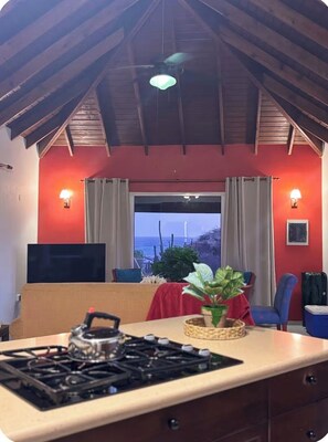 A kitchen with a gas stove, a dining table, and a view of the ocean through a large window.