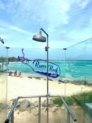 A beach view with a sign reading 'Rum Reef Aruba' and a metal structure with a light fixture.