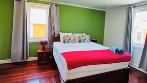 Quarto com cama, mesa de cabeceira, janela com cortinas e piso de madeira.