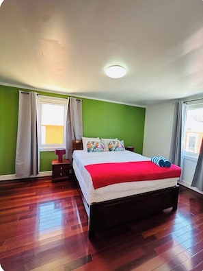 A bedroom with a bed, a nightstand, a window with curtains, and a wooden floor. - New 3BR 2BA with 2 Sofa Bed Baby Beach getaway-sleeps 9 (San Nicolas)
