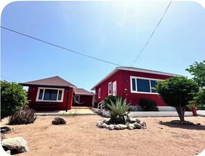 A two-story house with a red exterior and a brown roof, surrounded by a landscaped garden with rocks and plants.