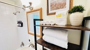 Un baño con ducha, lavabo, espejo y repisas con toallas y artículos de aseo.