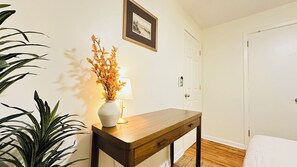 A room with a wooden table, a vase with yellow flowers, a framed picture on the wall, and a door.
