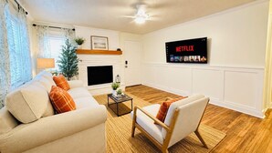A living room with a fireplace, a sofa, a chair, a coffee table, and a wall-mounted TV displaying Netflix.