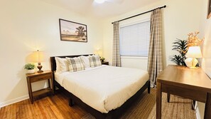 Een keurig opgemaakt slaapkamer met een bed, nachtkastjes, een bureau en een raam met gordijnen.