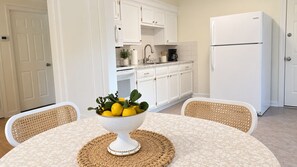 Een compacte keuken met witte kastjes, een witte koelkast en een eettafel met een geweven placemat.
