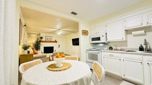 Cocina compacta con armarios blancos, microondas, estufa y comedor con mesa redonda y sillas.