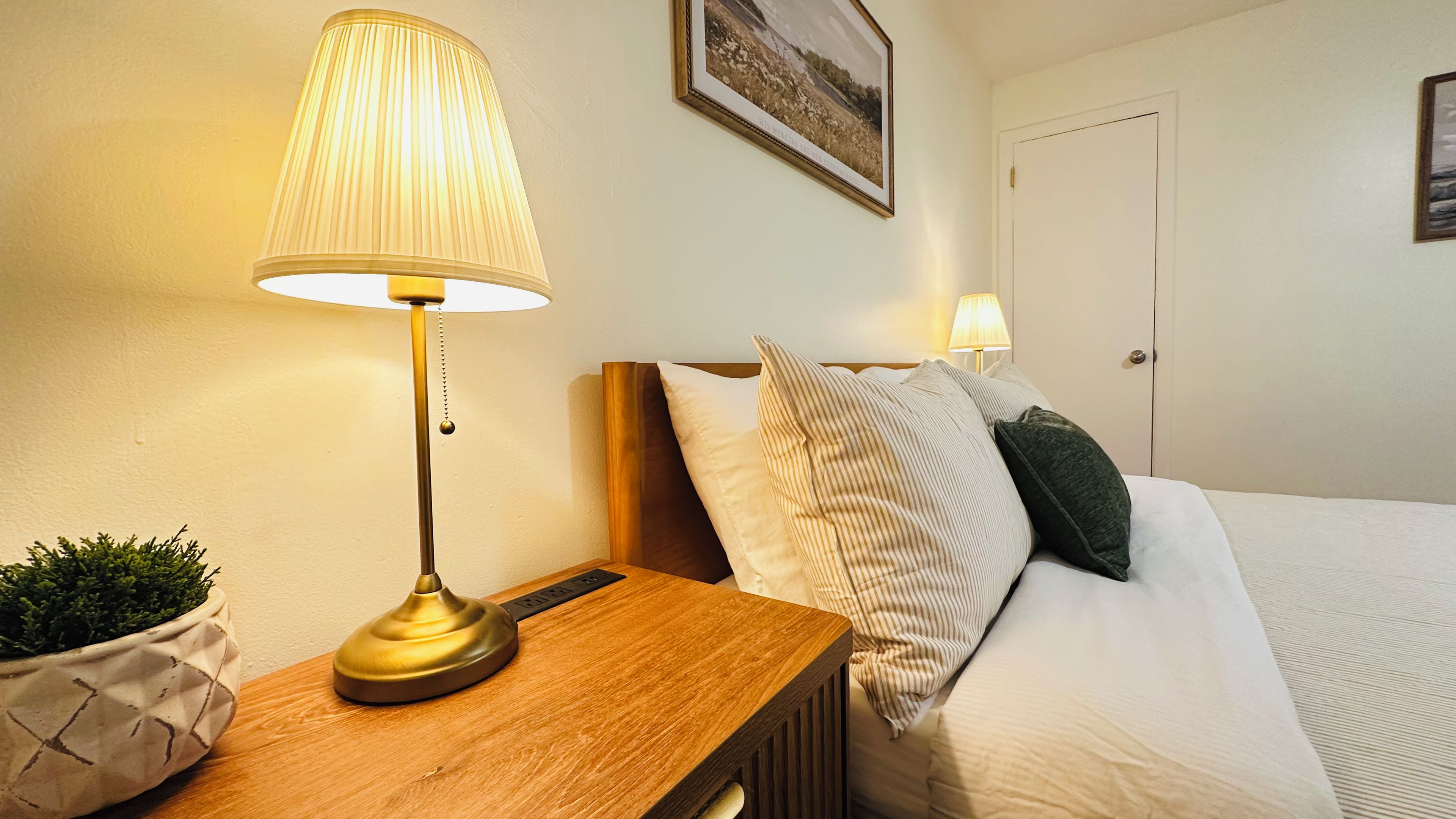 A neatly made bed with a wooden headboard, a bedside table with a lamp, and a framed picture on the wall.