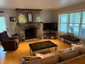 A living room with a stone fireplace, a television, a sofa, and a window with blinds. - Private Lakefront 3BR Retreat 2.5 Bath with private dock for your boat (Jay)