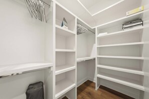 Un armari amb espai per a penjar i diverses prestatgeries, un sòl de fusta i un cubell de brossa visible.