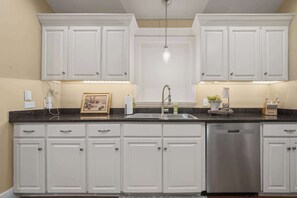 Una cocina con muebles blancos, lavavajillas de acero inoxidable y un lavamanos integrado.