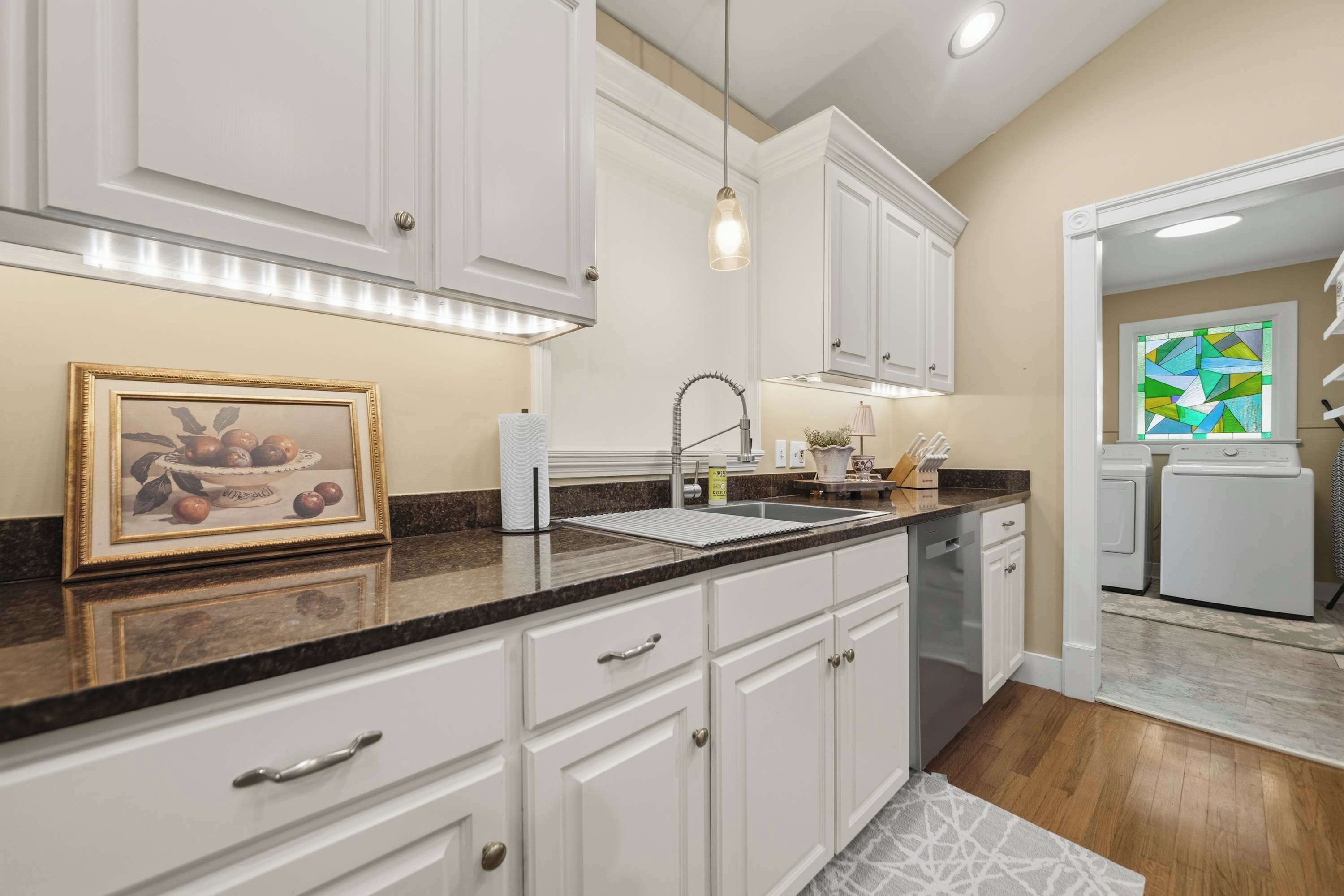 A kitchen with white cabinets, a granite countertop, a hanging pendant light, and a framed picture of fruit.