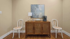 Une pièce comprenant un meuble en bois, deux chaises blanches, une machine à café et une lampe fixée au mur.